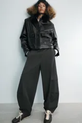 Chaqueta de efecto piel en color negro, con cuello de solapa con aplicación de pelo sintético, manga larga y bolsillos frontales de plastrón con solapa. Cierre frontal con cremallera y botones ocultos bajo solapa.