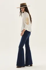 Camisa blanca de algodón con mangas abullonadas y puños fruncidos. Presenta bordados en tono beige/tostado a lo largo de la botonera frontal y un diseño bordado grande en forma de hoja o pluma en la manga.