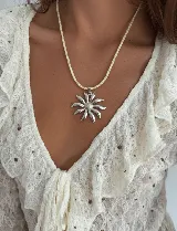 Collar con tiento estilo sailor de color crema y dije grande de acero quirúrgico en forma de flor o sol con centro texturizado.