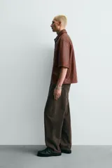 Sobrecamisa de corte relajado confeccionada en tejido efecto piel, con cuello solapa, manga corta, bolsillo plastrón en el pecho y cierre frontal con cremallera.