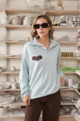 Buzo celeste de manga larga, cuello polo con botones y detalle de aplique marrón en el pecho.