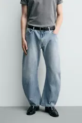 Jeans de denim de algodón en color negro con efecto lavado, corte amplio y silueta curva tipo barrel fit con pinzas en las rodillas. Presenta diseño clásico de cinco bolsillos y cierre frontal con cremallera y botón metálico.