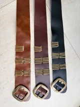Cinto tipo faja de cuero con hebilla metálica central y apliques decorativos de varillas metálicas verticales. Diseño estructurado ideal para definir la cintura.