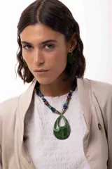 Collar corto con un gran medallón central de acrílico verde en forma de gota. La cadena está compuesta por una combinación de cuentas de acrílico, piedras naturales y cristales checos en tonos verdes, azules y marrones, con terminales metálicos.
