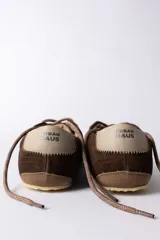 Championes urbanos de gamuza color marrón, con suela de goma en tono crema y cordones jaspeados. Presenta un refuerzo en la puntera y un detalle en cuero beige en el talón.
