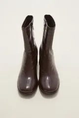 Bota corta de caña media en color negro, confeccionada en eco cuero con acabado brillante. Presenta cierre lateral interno, costura central decorativa en el empeine y taco cuadrado de altura media.