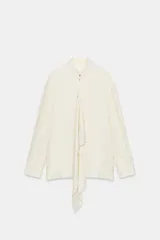 Blusa de viscosa color marfil, con cuello mao, manga larga con puños anchos, cierre frontal con botones y detalle de lazada colgante en el frente.