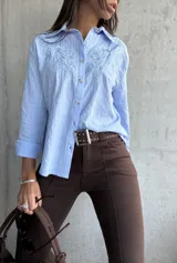 Camisa celeste de manga larga con cuello clásico, botones frontales y bordados florales en el pecho.