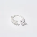 Anillo abierto de plata con diseño asimétrico, decorado con cristales en talla baguette en un extremo y un cristal en talla gota en el otro.