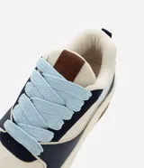 Championes casuales de estilo urbano con diseño de paneles en colores azul marino, beige y celeste. Presentan suela tipo caja de goma color crema con base marrón, cordones gruesos en color celeste y lengüeta acolchada.