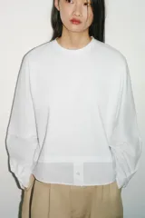 Camiseta oversize de cuello redondo y manga larga con puños abotonados. Confeccionada en algodón, presenta un diseño con combinación de tejidos a tono y bajo asimétrico.