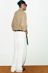Chaqueta corta marrón de cuello solapa y manga remangada por debajo del codo. Presenta bolsillos delanteros de plastrón con solapa, bajo ajustable con cordón interior y cierre frontal con botones.