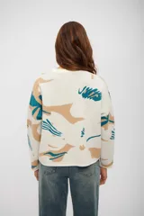 Buzo de tejido de punto con diseño estampado abstracto en tonos beige y turquesa sobre base color crudo, de corte holgado, cuello redondo y mangas largas.
