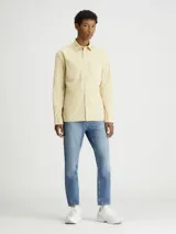 Camisa de manga larga color beige claro, con cierre frontal de botones, doble bolsillo en el pecho y logo pequeño en uno de los bolsillos.