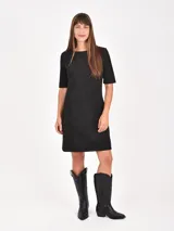 Vestido corto de corte recto y estilo minimalista, confeccionado en tela tipo gamuza negra. Presenta cuello redondo, mangas cortas y dos bolsillos frontales aplicados a la altura de la cadera.