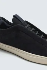 Zapatilla urbana de hombre confeccionada en piel con acabado de serraje, diseño minimalista con cordonera oculta y suela de goma a contraste.