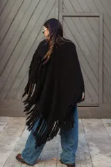Poncho triangular de lana en color crudo, con diseño de tejido texturizado y terminaciones de flecos largos en todo el borde.
