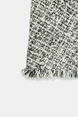 Falda corta de tiro medio confeccionada en tejido de tweed con textura, en tonos blanco y negro. Presenta pinzas en el delantero, bajo con terminación desflecada y cierre lateral con cremallera oculta.