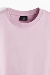 Remera de punto de algodón de peso medio en color lila, con cuello redondo ribeteado, hombros caídos y bajo recto. Diseño de corte relajado y silueta casual.