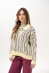 Buzo de punto tipo polo en tono amarillo claro con diseño de ondas a rayas en tonos marrón y celeste. Presenta cuello clásico, cierre frontal parcial con botones y silueta relajada con mangas largas.