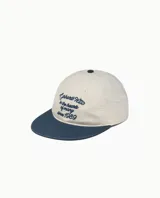 Gorra de béisbol de cinco paneles, color crema con visera azul marino. Presenta bordado en el frente con el texto "Carhartt WIP in the hearts of many since 1989" en hilo azul.