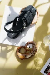 Sandalias de cuero negro con diseño de tiras entrelazadas, estilo huarache, con pulsera ajustable al tobillo mediante hebilla metálica.