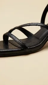 Sandalias de cuero negro con tiras cruzadas en el empeine y cierre de hebilla en el tobillo. Presentan un diseño de punta cuadrada y taco bloque de altura media.