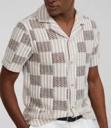 Camisa de manga corta con cuello inglés y abotonadura frontal. Diseño con encaje bicolor texturizado en tonos beige y blanco. Corte regular.