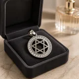 Dije circular de acero con diseño de Estrella de David calada en el centro, rodeado por un borde engastado con circonias brillantes.