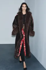 Abrigo largo de terciopelo en tono marrón oscuro, con cuello solapa y puños adornados con aplicación de pelo sintético. Presenta un diseño abierto con forro interior en color rojo con estampado floral.