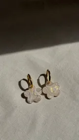 Aros colgantes con argollas doradas de acero quirúrgico y dijes de acrílico con forma de flor, en tonos beige y dorado con efecto marmolado o iridiscente.