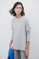 Remera de manga larga en color beige, con cuello redondo y costuras visibles estilo raglán. Presenta un corte holgado y un pequeño bordado distintivo en el ruedo inferior.