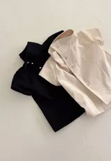 Top de algodón color crema, de manga corta y cuello alto estructurado. Cuenta con cierre frontal cruzado con botones metálicos a presión y costuras decorativas.