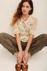 Sweater de tejido calado color beige, con escote en V y mangas cortas abullonadas. Presenta un delicado bordado floral multicolor en la parte frontal superior.