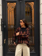 Cardigan tejido con diseño de rombos en tonos marrón y negro, escote en V y cierre frontal de botones con efecto carey. Presenta mangas largas y corte holgado.