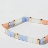 Pulsera elástica con cuentas rectangulares de colores pastel (blanco, celeste y salmón) separadas por cuentas doradas.