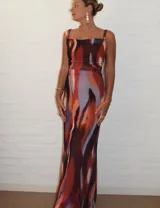Vestido largo de microtul estampado con diseño abstracto en tonos marrones, naranjas y celestes. Tiene breteles finos y corte ajustado al cuerpo.