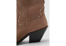 Botin de estilo western confeccionado en piel bovina, con diseño de caña media, punta fina y detalle de tachas metálicas decorativas en el empeine. Cuenta con un pequeño taco cuadrado y suela de caucho.