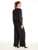 Blusa negra de gasa translúcida con diseño de líneas verticales texturizadas y sutiles aplicaciones de lentejuelas. Presenta cuello a la base, cierre frontal con botones, mangas largas estilo balloon con puños abotonados y ruedo elastizado.