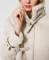 Chaqueta color beige de napa y piel sintética con cuello con cierre de hebilla y almeja, mangas largas con hombros caídos, tirantes en los puños, cierre de cremallera oculta, bolsillos laterales, cierre de hebilla y almeja en el dobladillo y placa en T ovalada en la parte posterior.