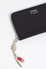 Billetera Bimba y Lola de cuero sintético color beige, con cierre perimetral y logo grabado en letras doradas. Incluye un tirador de cierre con cordón rojo y detalles de cuentas.