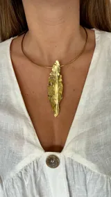 Gargantilla dorada rígida con dije colgante en forma de hoja texturada.