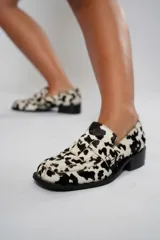 Mocasín de cuero con pelo y estampado de vaca en blanco y negro. Presenta horma cuadrada, diseño enrejillado en la capellada y taco bajo de 4,5 cm.