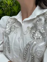 Camisa blanca de mangas 3/4 con bordados de lentejuelas y mostacillas plateadas en el frente.