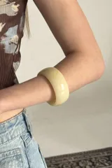 Brazalete rígido de resina en color marfil, de diseño ancho y acabado brillante.