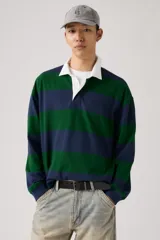 Remera tipo rugby de manga larga con diseño de rayas horizontales anchas en azul marino y verde. Presenta cuello polo en color blanco con tapeta de botones oculta y puños acanalados.