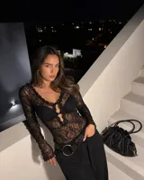 Body de encaje negro con mangas largas, escote profundo con detalle de abertura frontal y cierre de ganchos. Diseño ajustado al cuerpo con textura floral.