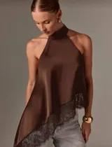 Blusa de seda color marrón oscuro, estilo halter con cuello alto fruncido. Presenta un corte asimétrico y un ruedo con terminación de encaje.