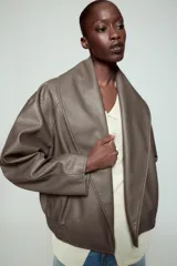 Cazadora Zara Woman Collection de efecto piel con cuello solapa ancho, manga larga, bolsillos delanteros y bajo elástico. Presenta un cierre frontal cruzado con botón a presión.