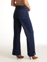 Jean wide leg azul oscuro de tiro alto, con pierna ancha y ruedo con tajo lateral. Presenta pretina con pasadores, botón y cierre, y bolsillos delanteros y traseros.